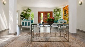 Une pièce spacieuse avec une table au centre, deux chaises, une plante en pot et une porte donnant sur un autre espace.