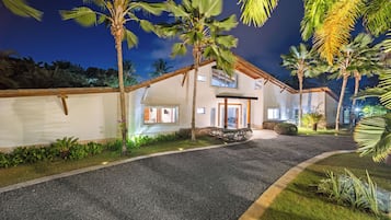 A two-story house with a gravel driveway, surrounded by palm trees and a well-maintained lawn.