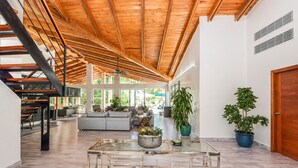 Un intérieur spacieux avec un plafond haut, un escalier, un coin salon avec un canapé et des plantes en pot.