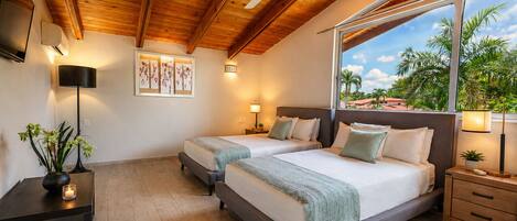 A double room with two beds, a ceiling fan, a large window with a view, and a small table with a lamp.