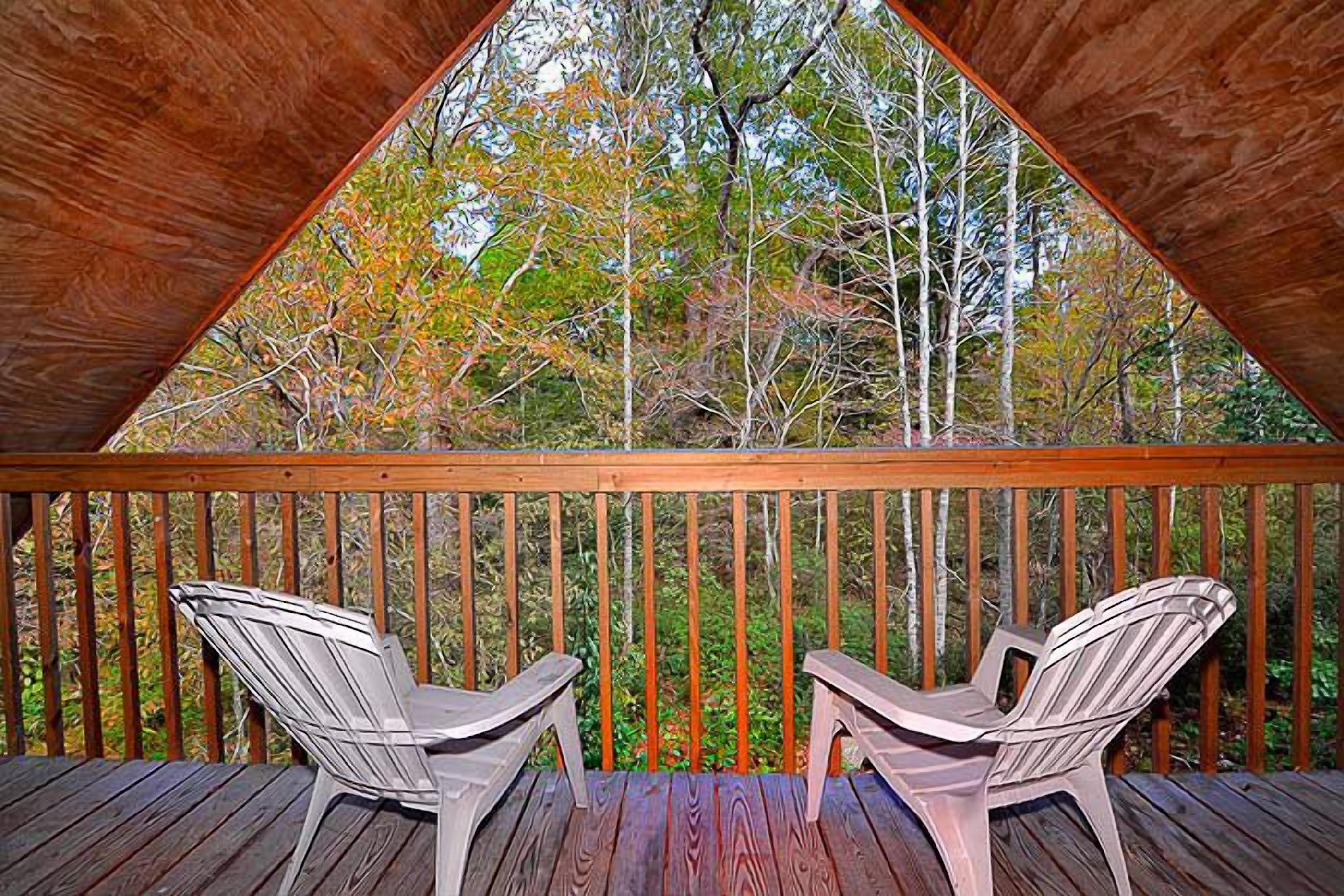 Eine Holzterrasse mit zwei Adirondack-Stühlen, die auf einen Wald blicken.