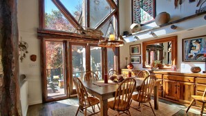 Un comedor con mesa y sillas de madera, ventanas amplias y vistas al exterior.