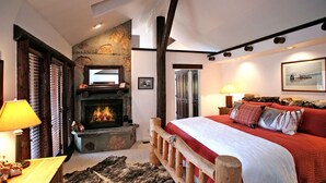 Un dormitorio acogedor con chimenea, una cama con ropa de cama roja, un cabecero de madera y una alfombra rústica.