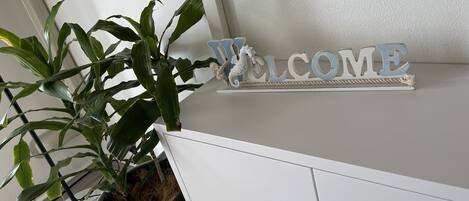A white reception desk with a potted plant, a 'WELCOME' sign, and a decorative rope border.