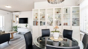 A modern living room with a glass dining table surrounded by black chairs, a white cabinet with glass doors, and a flat-screen TV mounted on the wall. - Balmoral Escape - footsteps from beach (Mosman)