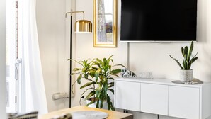 A modern living room with a flat-screen TV mounted on the wall, a white cabinet below, and a wooden dining table with a potted plant. - Balmoral Escape - footsteps from beach (Mosman)