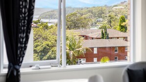A hotel room with a large window offering a view of a hillside and buildings. - Balmoral Escape - footsteps from beach (Mosman)