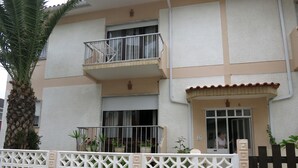 Un immeuble de deux étages doté d’un balcon, d’une entrée fermée par un portail et d’un palmier.