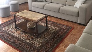 Un salon avec un canapé gris, une table basse en bois, un tapis à motifs et un tableau accroché au mur.