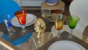 Un coin repas avec une table dressée pour quatre personnes, agrémenté d’un ensemble de verres bleus et rouges, d’un bol décoratif doré et d’une assiette blanche.