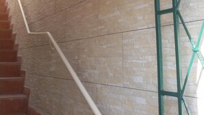 Un escalier avec une rampe blanche, un mur en pierre beige et un portail en métal vert.