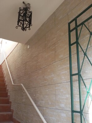 Una escalera con barandilla blanca, pared de piedra color beige y una verja metálica verde.
