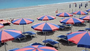 Une plage avec de nombreux parasols rayés de rouge et de bleu, ainsi que des chaises longues bleues.