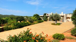 Eine weiße Villa mit gepflasterter Auffahrt, umgeben von üppigem Grün und blauem Himmel.