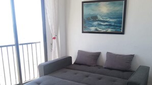 A modern bedroom with a grey sofa bed, a painting of the sea, and a view through a large window. - Apartment/ flat - DeniaResidential flat (Denia)