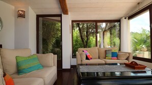 A modern living room with two beige sofas, colorful cushions, a black coffee table, and large windows offering a view of greenery outside. - Exceptional luxury house, poolhouse area and heated swimming pool (Seillans)