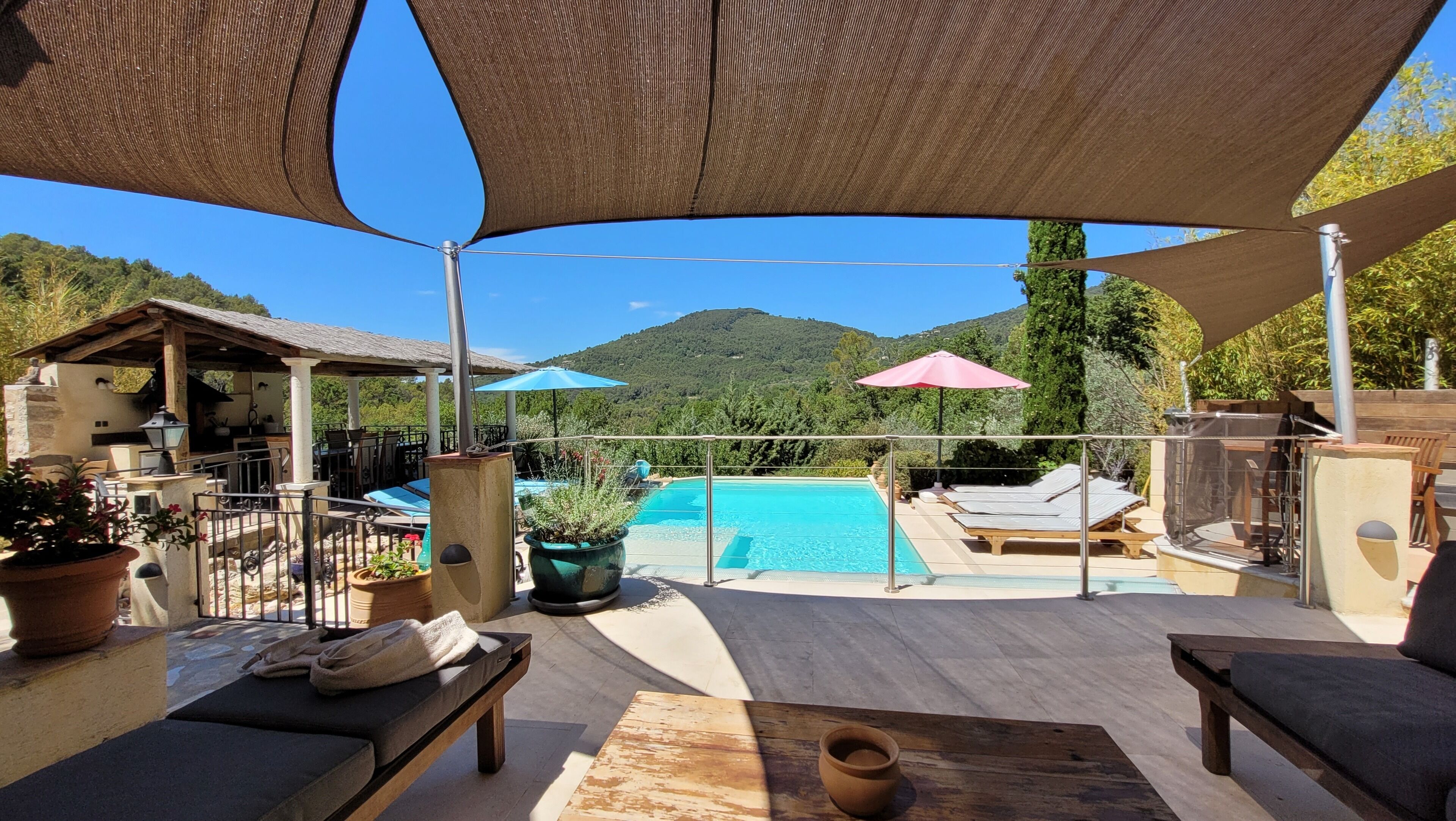 A poolside area with a view of a mountain, outdoor seating, and umbrellas.