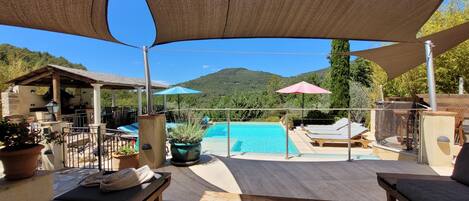 A poolside area with a view of a mountain, outdoor seating, and umbrellas.