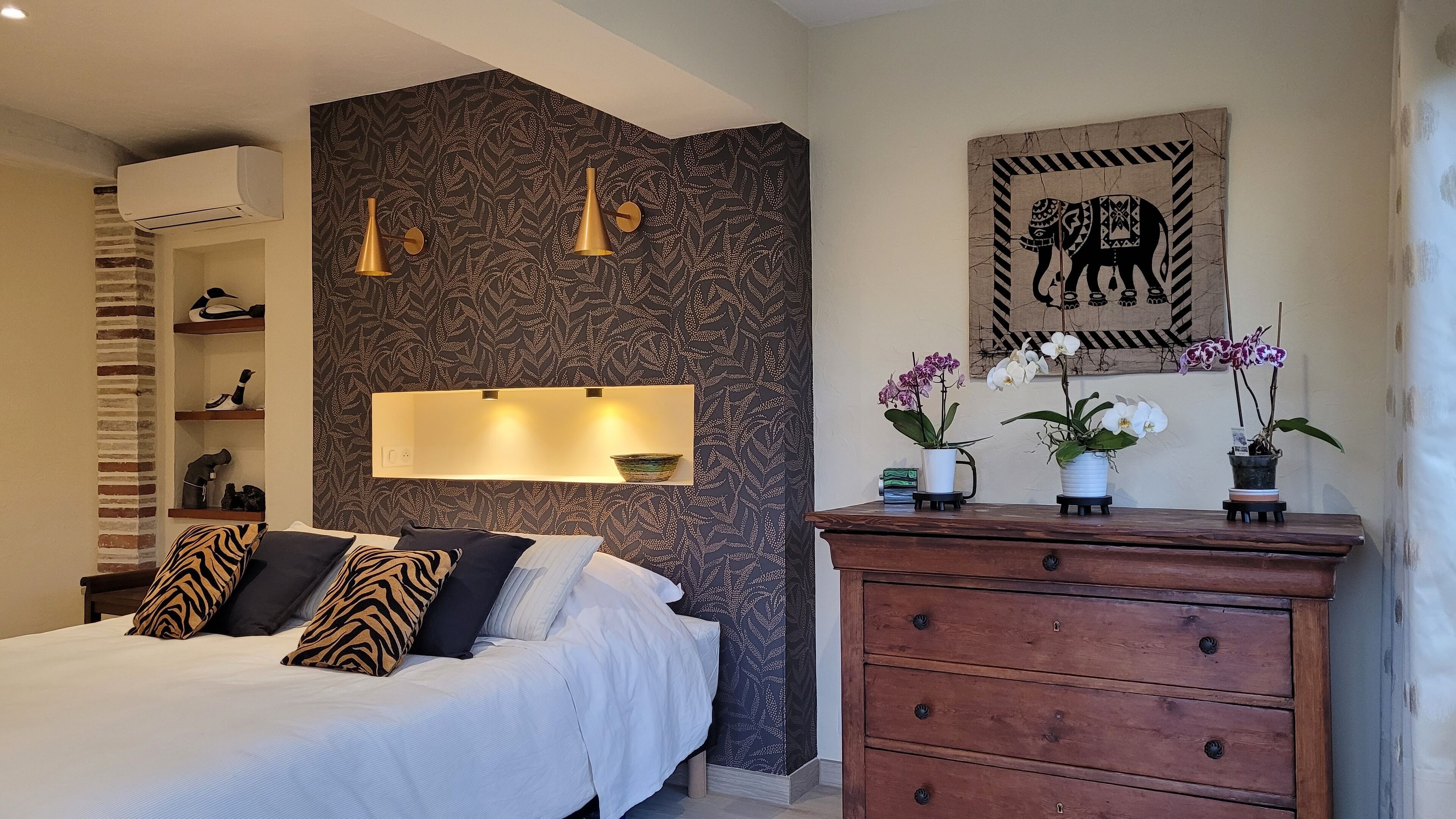 Un dormitorio con cama, mesitas de noche, cómoda, estante en la pared y un cuadro decorativo de un elefante.