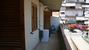 A narrow balcony with a white refrigerator, wooden shutters, and a view of a residential building with balconies. - apartment 300 meters from the sea (Follonica)
