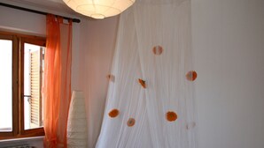 A bedroom with a bed covered in white sheets, a large window with orange curtains, and a white canopy with orange flowers. - apartment 300 meters from the sea (Follonica)
