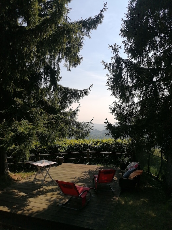 An outdoor deck with a table and chairs, surrounded by trees and a view of distant hills.