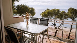 A balcony with a table and chairs, overlooking a beach with trees and a clear sky. - Agi Marina 8 Apartamento for rent in Roses Girona. (Rosas / Roses)