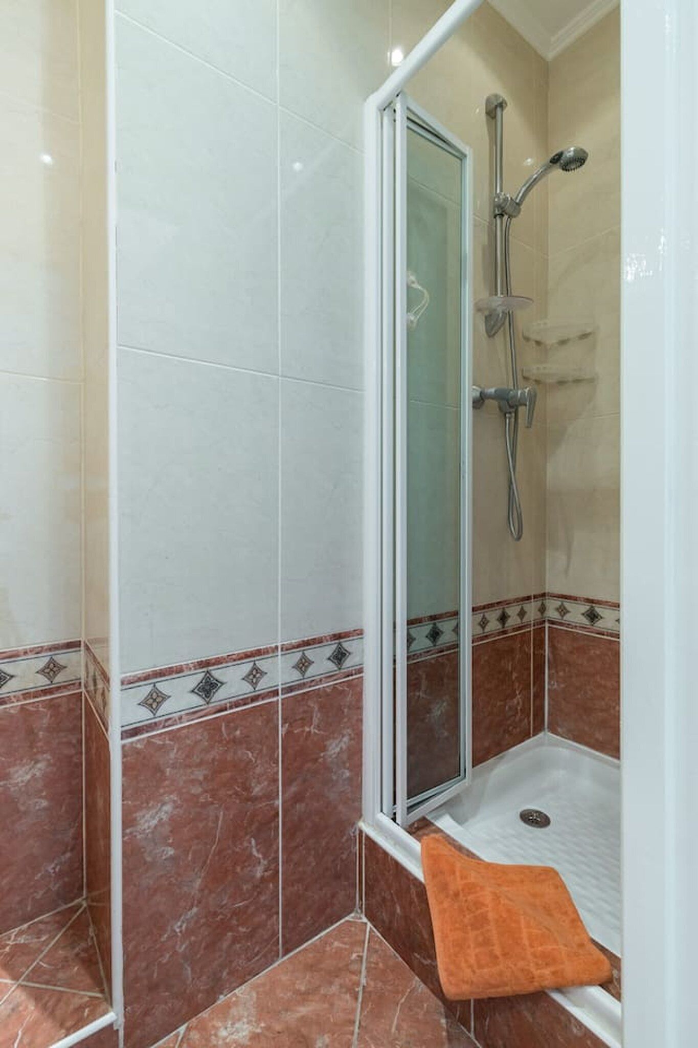 A shower area with a glass door, a handheld showerhead, and a handheld showerhead with a brush attachment.