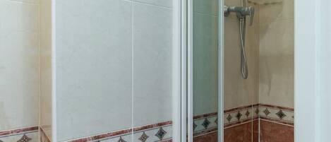 A shower area with a glass door, a handheld showerhead, and a handheld showerhead with a brush attachment.