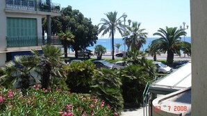 A balcony with a view of the sea, palm trees, and parked cars. - WATERFRONT PANORAMIC Seaview 2bd/2bath Apt on Promenade Des Anglais by Negresco  (Nice)