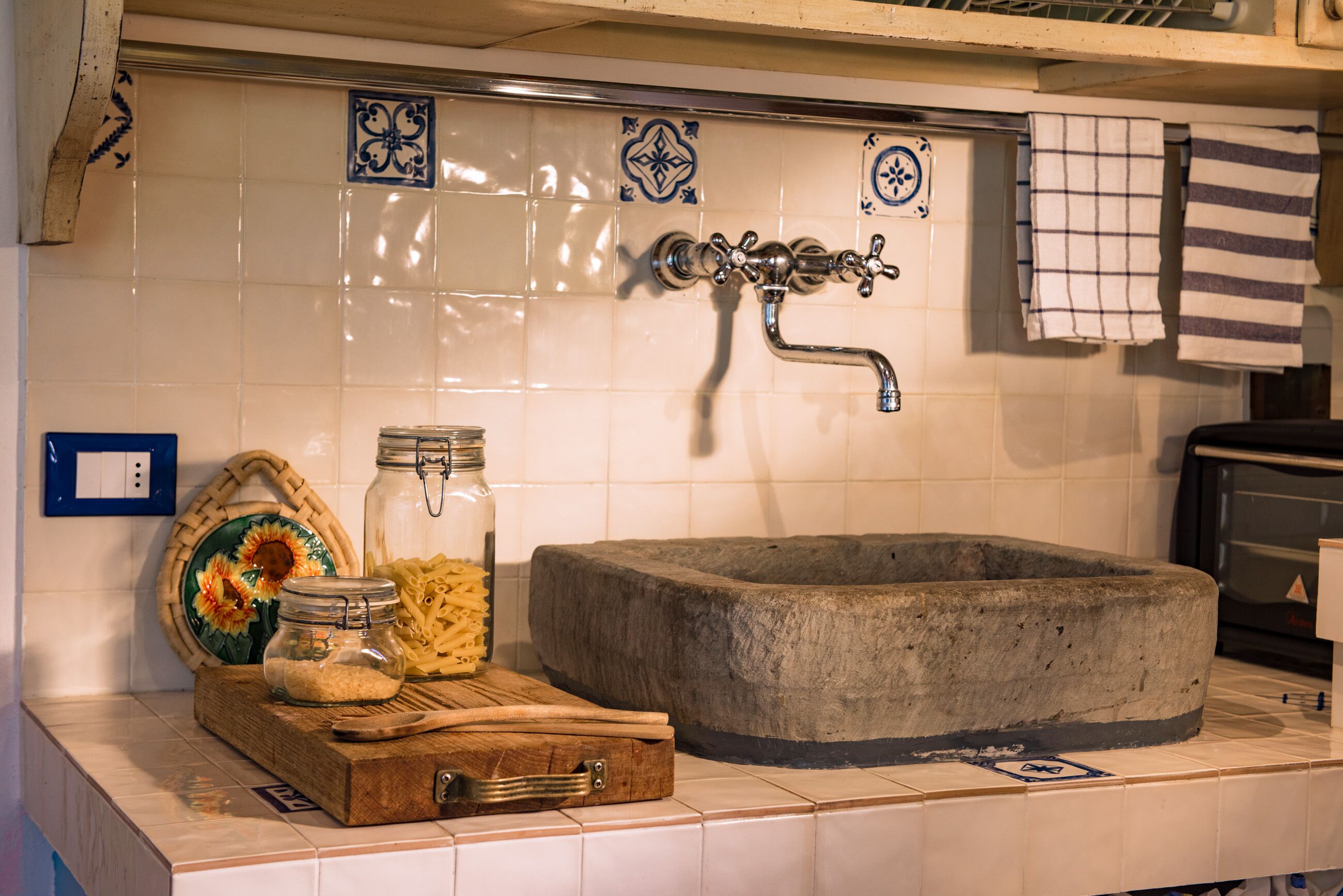 A kitchen with a stone sink, a wooden cutting board, a glass jar, and a metal faucet.