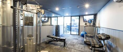 Une salle de sport équipée de machines de musculation, d’un banc, d’haltères et d’un tapis de course.