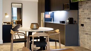 A modern kitchen with a round dining table, two chairs, a coffee machine, and a TV mounted on the wall.