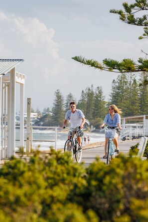 A wooden boardwalk with two people riding bicycles, overlooking a beach and ocean. - The Sebel Brisbane Margate Beach (Margate)