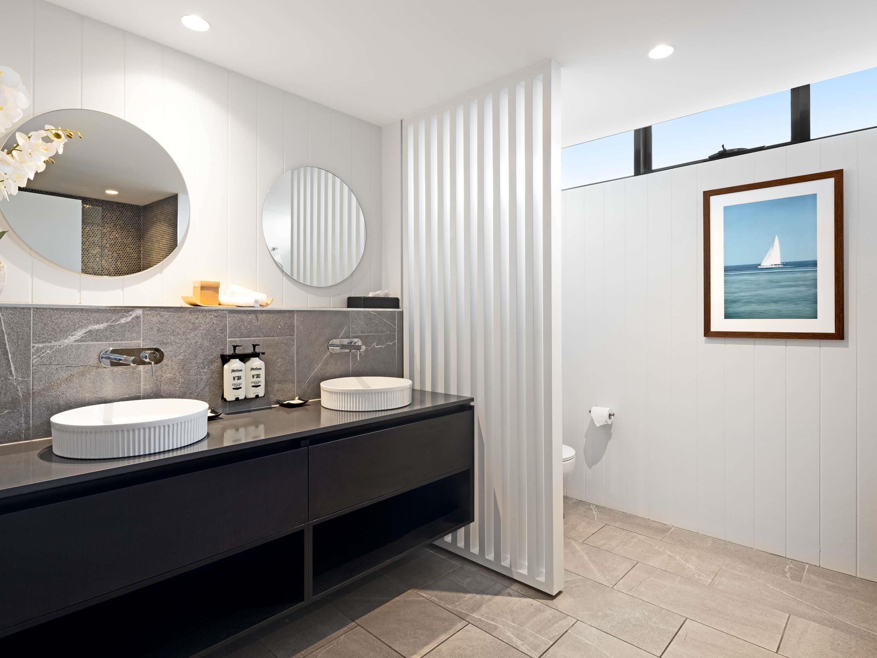 A modern bathroom with two sinks, a large mirror, and a framed picture on the wall.