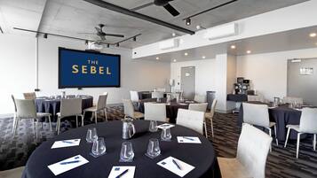 Un salón de conferencias con mesas redondas, sillas y una gran pantalla que muestra "THE SEBEL".