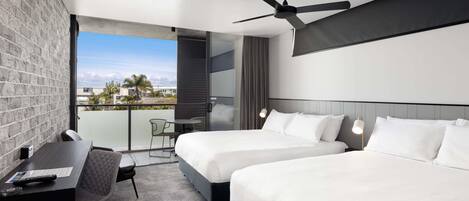 Una habitación de hotel moderna con dos camas, un escritorio, una silla, un ventilador de techo y un balcón con vistas.