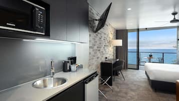 Habitación de hotel moderna con cocina, cama, escritorio y vista al mar.