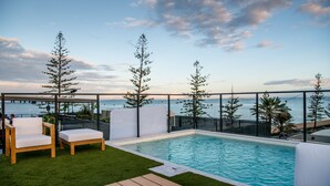 A rooftop pool area with a view of the ocean, surrounded by wooden furniture and a wooden deck. - The Sebel Brisbane Margate Beach (Margate)