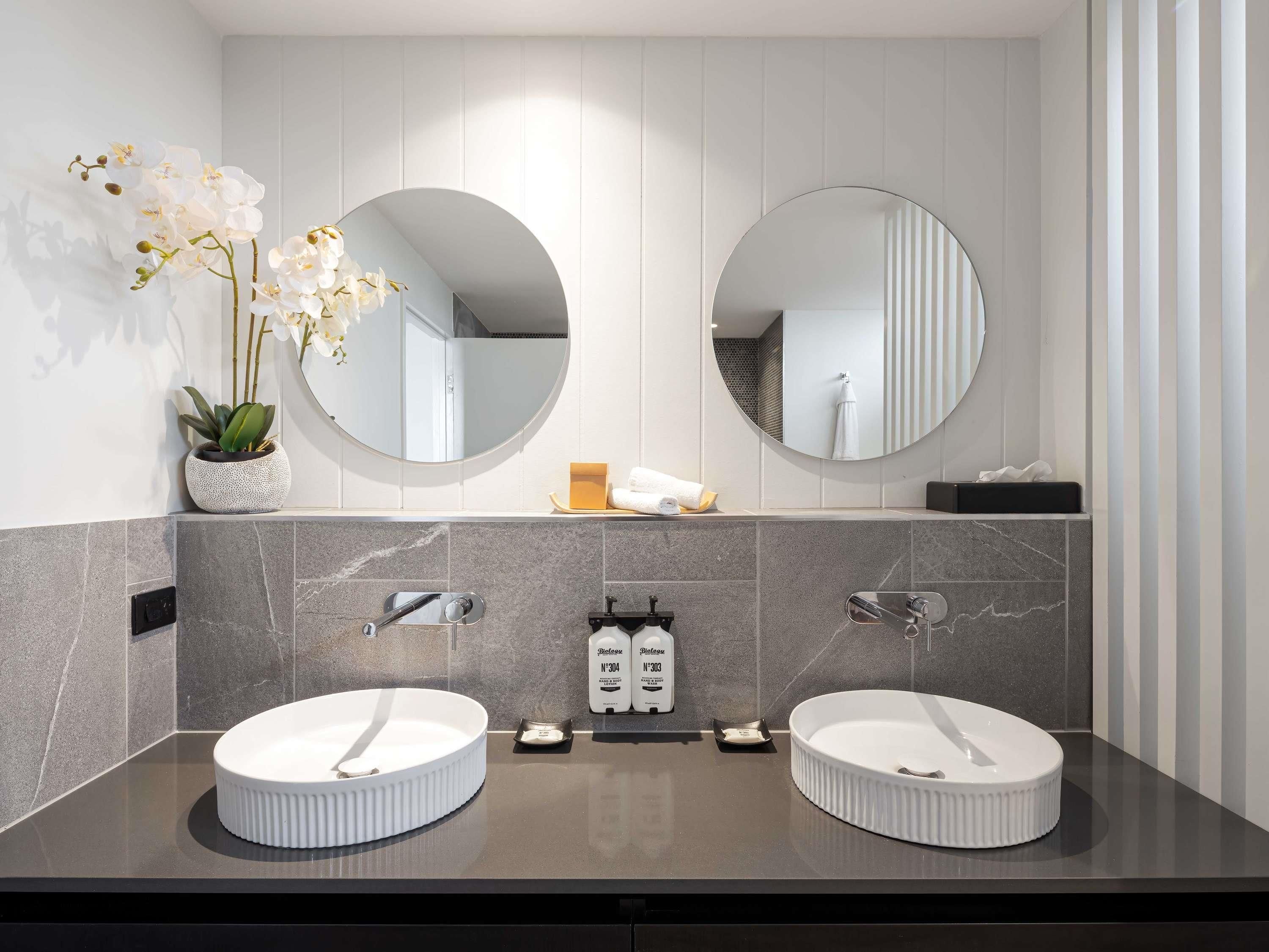 Un baño moderno con dos lavamanos, una orquídea en maceta y un espejo.
