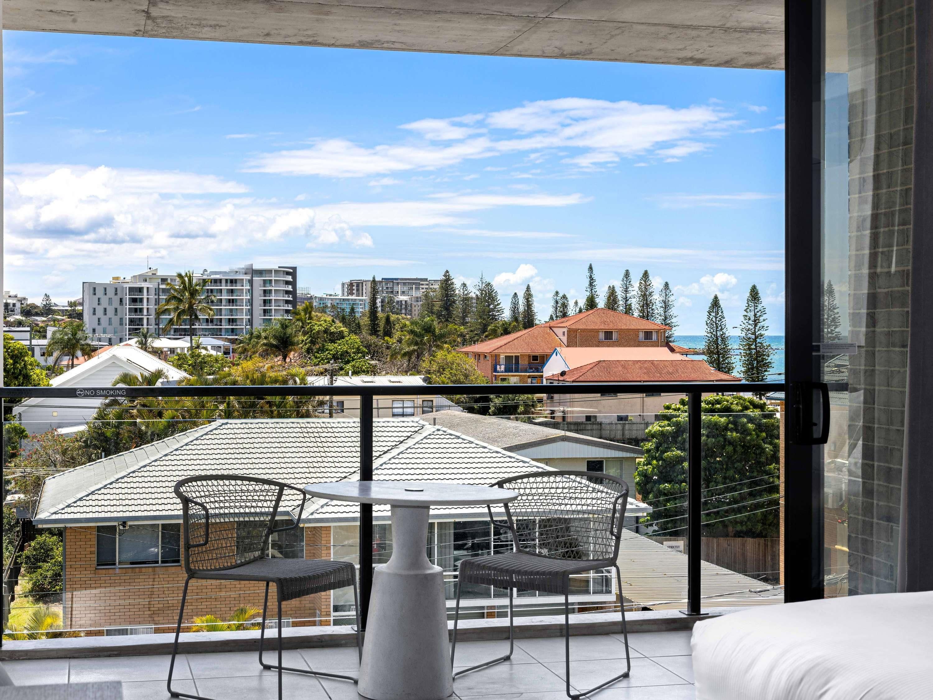 A balcony with a table and chairs, overlooking a residential area with houses and trees.