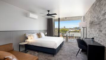 A modern hotel room with a large bed, a desk, and a balcony with a city view.