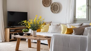 Un salon avec une télévision, une table basse en bois, un canapé avec des coussins et une fenêtre avec des rideaux.