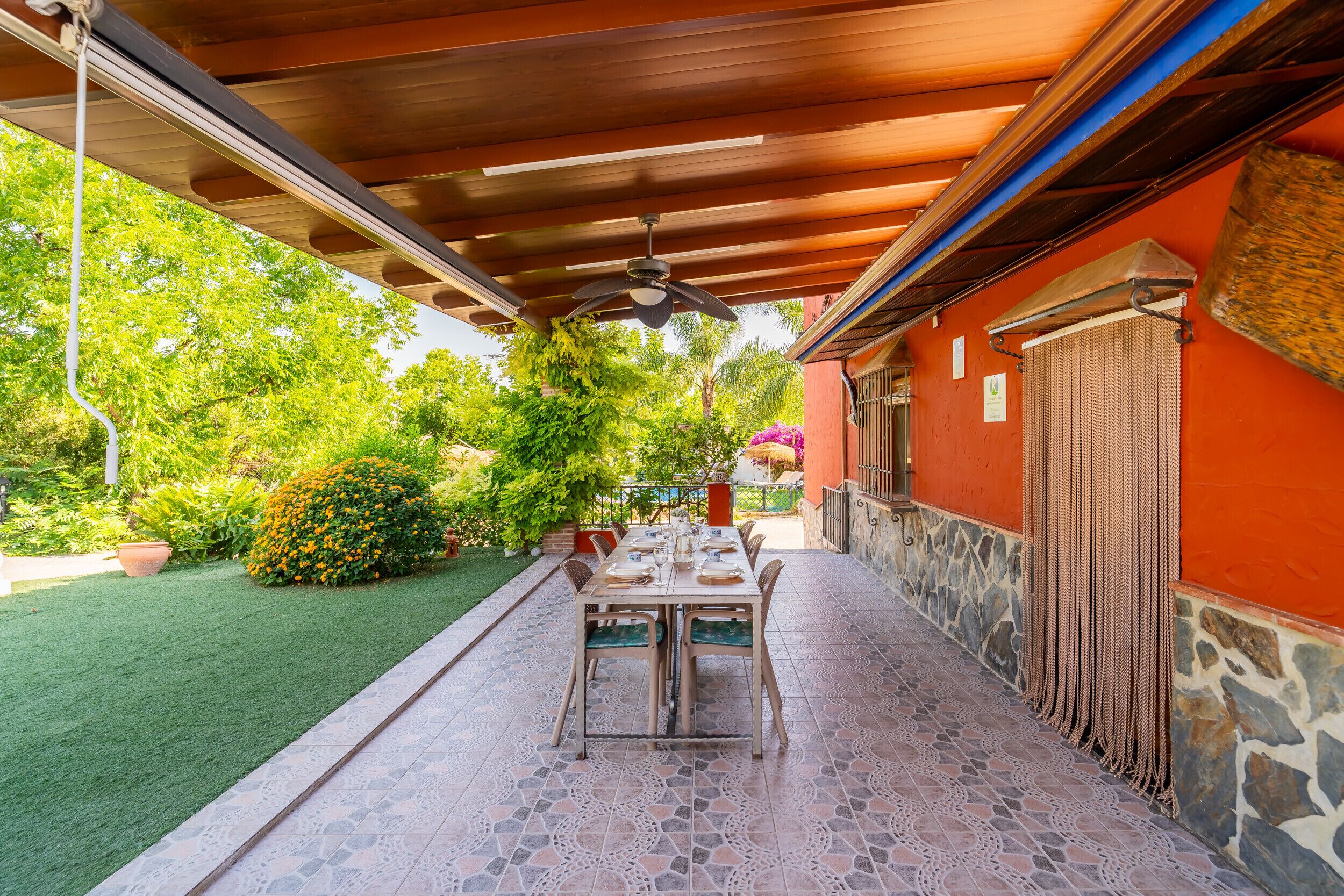 An outdoor patio with a table and chairs, a ceiling fan, and a garden with various plants.