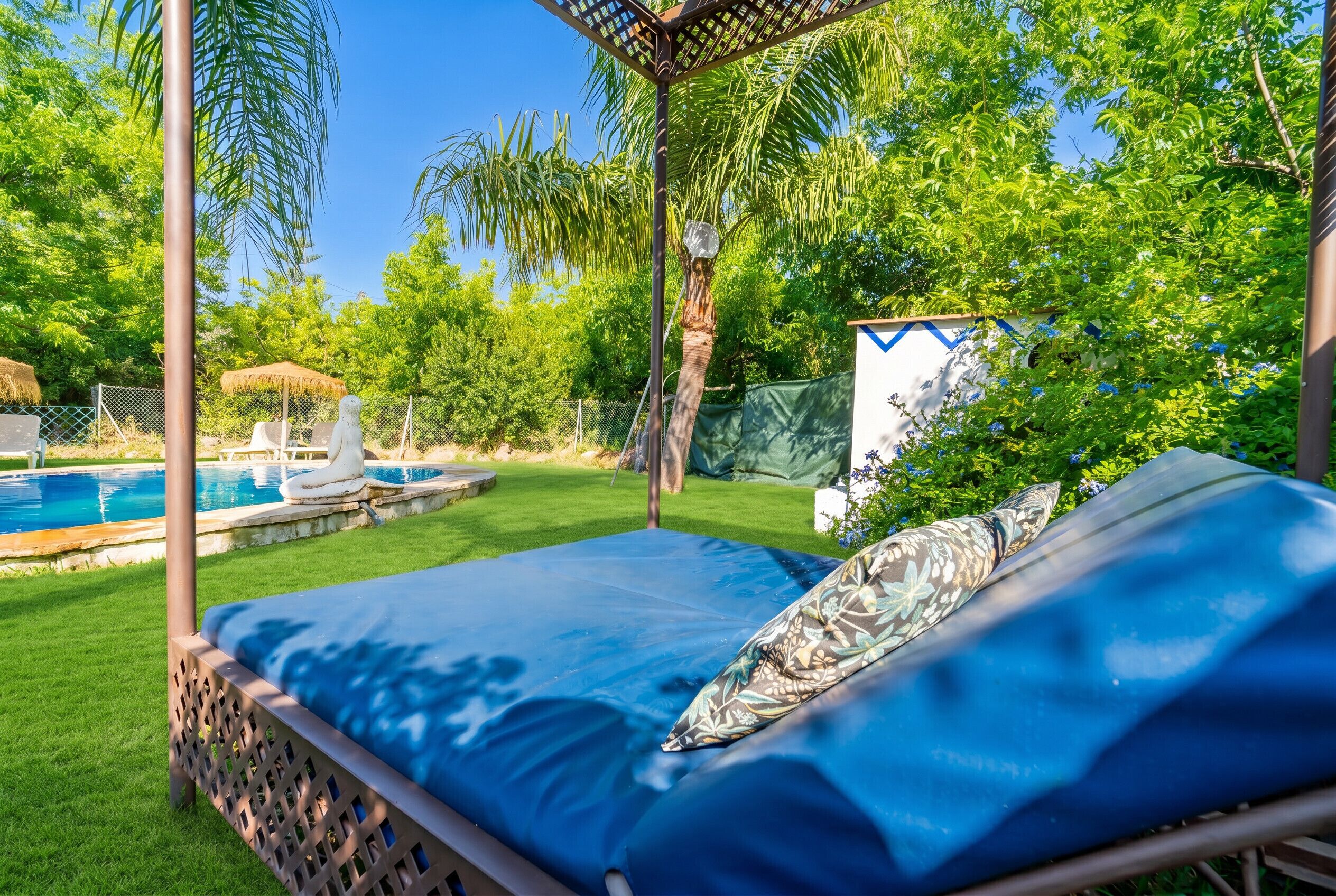 A poolside lounge area with a bed, a pergola, and a small shed.