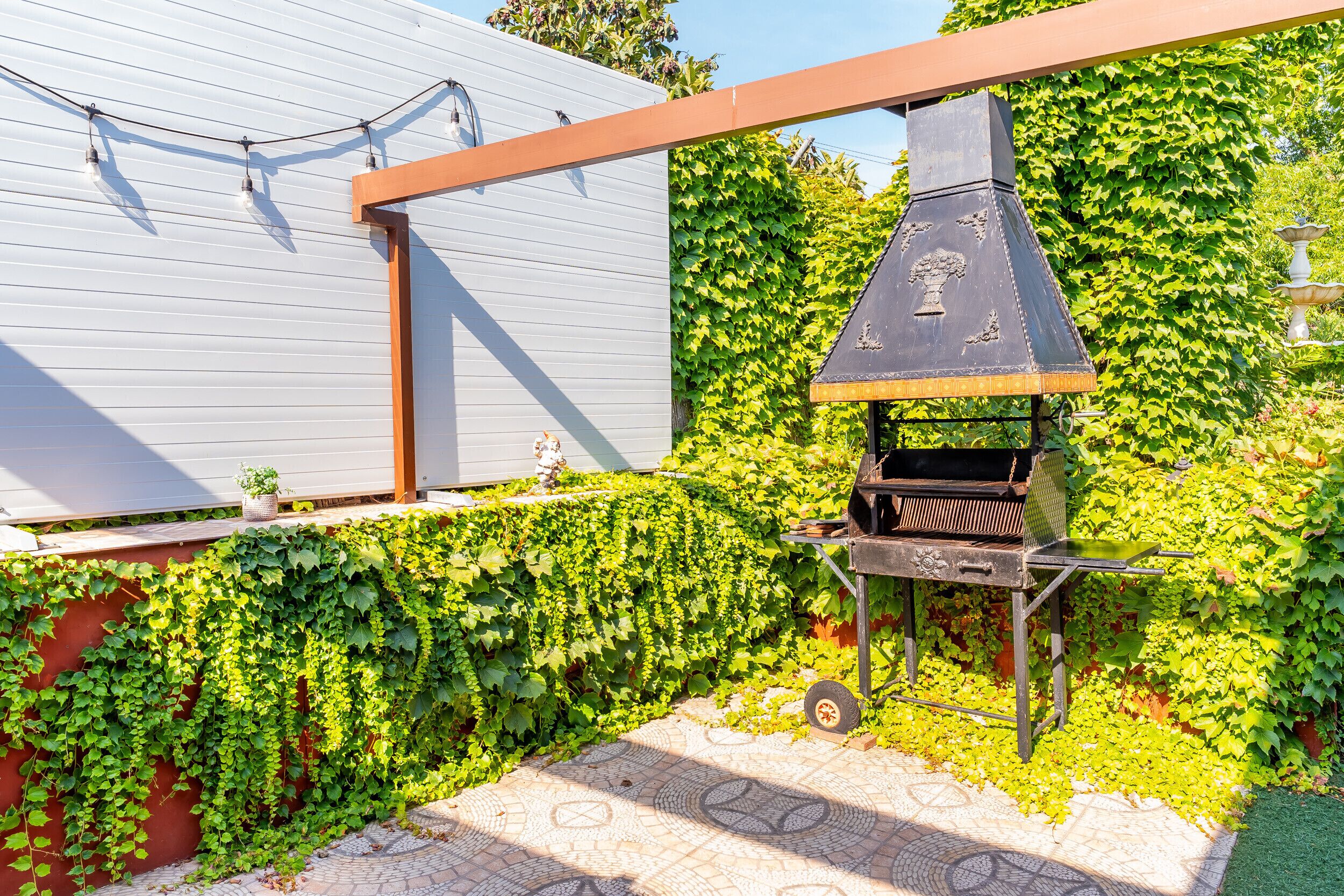 En grill med skorsten, en fliseterrasse og en mur dækket af efeu.