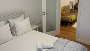 A bedroom with a bed, a bedside table, a door leading to a living area, and a ceiling light. - Romantic Alfama - Duplex Apartment in Lisbon, Alfama (Lisboa)