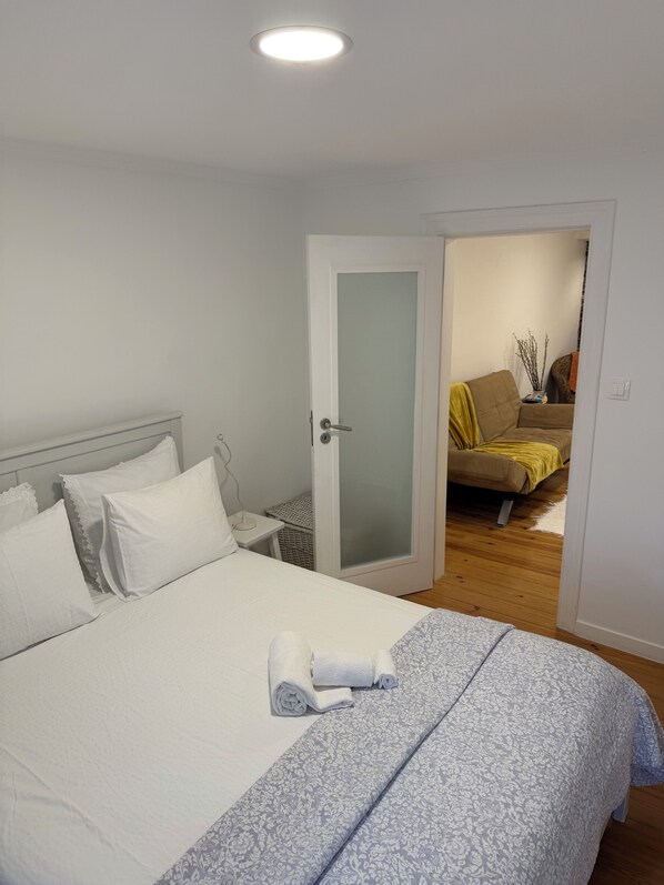 Ein Schlafzimmer mit Bett, Nachttisch, einer zur Wohnbereich führenden Tür und einer Deckenleuchte.