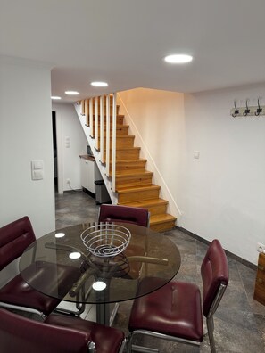 A modern interior with a glass table surrounded by leather chairs, a wooden staircase, and a coat rack.