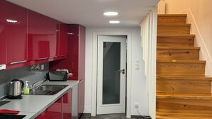A modern kitchen with red cabinets, a stainless steel sink, and a wooden staircase. - Romantic Alfama - Duplex Apartment in Lisbon, Alfama (Lisboa)